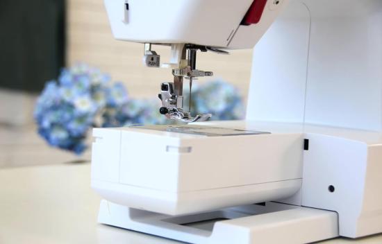 Nahaufnahme einer modernen weißen Nähmaschine mit unscharfen blauen Blumen im Hintergrund