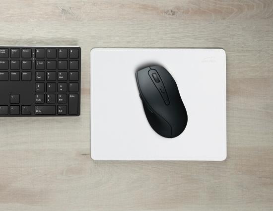 Schwarze kabellose Maus auf weißem Mauspad, links daneben eine schwarze Tastatur auf Holztisch